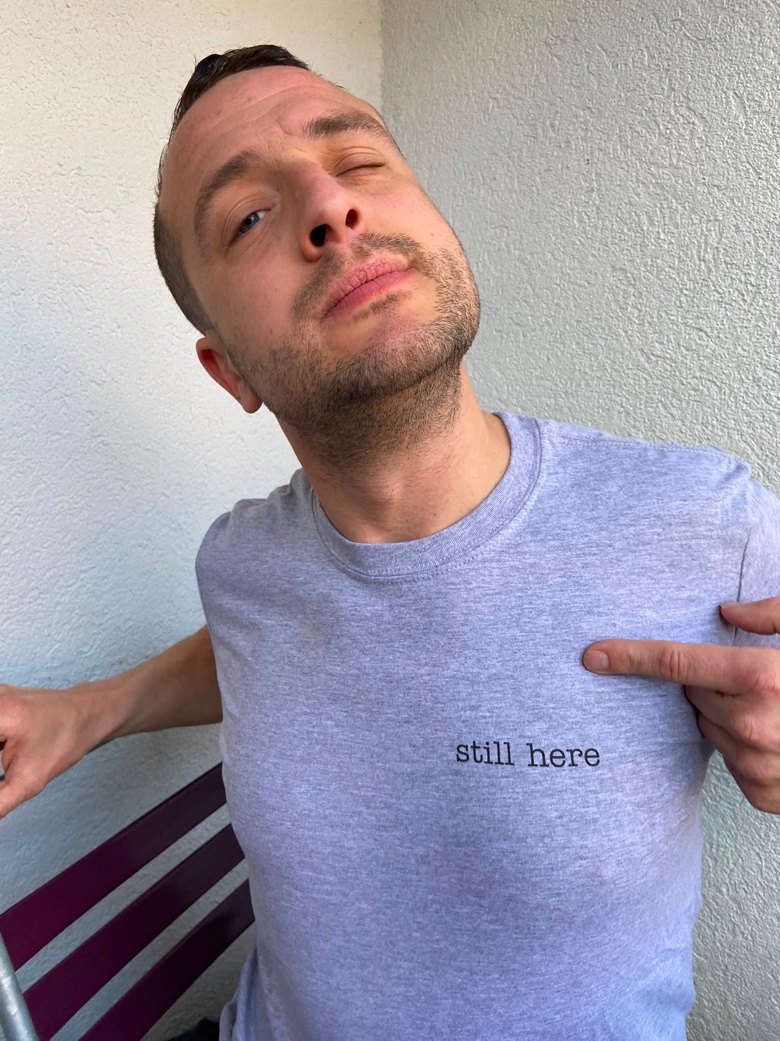 Dizzy zeigt auf sein Shirt: still here